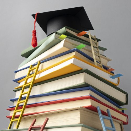 angulo-libros-apilados-gorro-graduacion-escaleras-dia-educacion (1)
